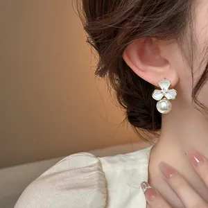 Detailed view of elegant white flower earrings with rhinestone center and pearl drop.