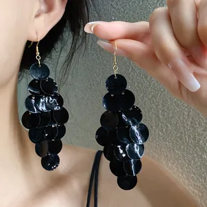 Détail de boucles d'oreilles pendantes à pampilles en nacre noire portées et tenues
