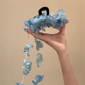 Gedetailleerde weergave van haarklem met blauwe stoffen bloemen en parelmoer kwastjes.
