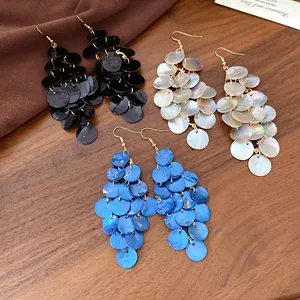 Gros plan sur des boucles d'oreilles bohèmes en nacre de couleurs noir, blanc et bleu.