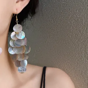 Gros plan de boucles d'oreilles frangées en nacre avec pièces circulaires sur modèle