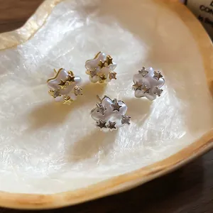 Detailed view of star pearl and zircon earrings displayed inside a decorative shell tray