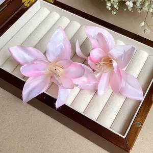 Gros plan de pinces à cheveux en forme de lys en tissu rose dans une boîte à bijoux en bois.