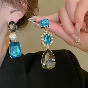 Primer plano de elegantes pendientes largos con cristales azules y grises y perlas