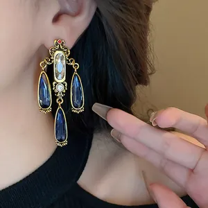 Dettaglio di orecchini pendenti barocchi dorati con cristalli blu a forma di goccia