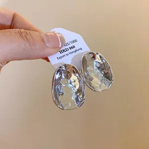Nahaufnahme von silberfarbenen, unregelmäßig faltigen Ohrsteckern auf weißer Verpackung