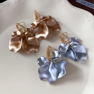 Primo piano di eleganti orecchini pendenti in metallo dorato e blu a forma di petalo su piatto