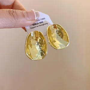 Nahaufnahme von goldfarbenen, gehämmerten, unregelmäßigen Ohrsteckern mit Textur