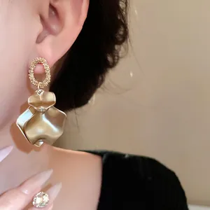 Primo piano di eleganti orecchini a petalo d'oro opaco con maglia ovale testurizzata.