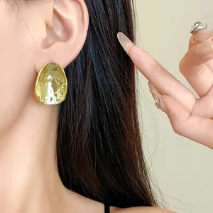 Nahaufnahme von minimalistischen, unregelmäßigen goldfarbenen Ohrringen an einem Ohr.