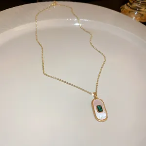 Close-up of elegant gold necklace featuring an emerald green zircon on a shell pendant.