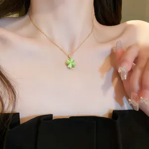 Detailed close-up of a green four-leaf clover pendant necklace with a gold chain on neck