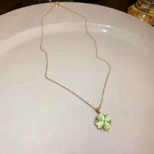 Close-up of a gold necklace with a light green four-leaf clover pendant on a white plate