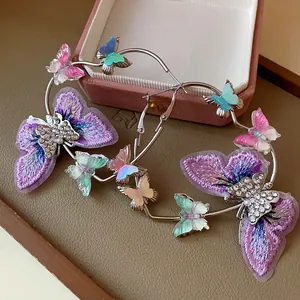 Detailed shot of large silver hoop earrings with embroidered and rhinestone butterflies.