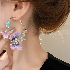 Detailed view of heart-shaped hoop earrings with colorful butterfly charms on model's ear.