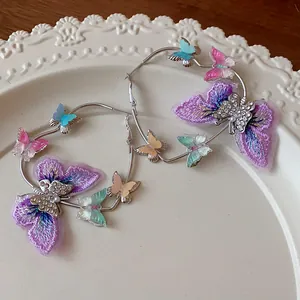 Detail view of large hoop earrings decorated with embroidered and acrylic butterflies