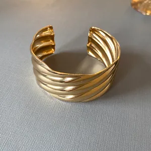 Close-up of fashion golden metal cuff bracelet featuring bold wave texture and open design.