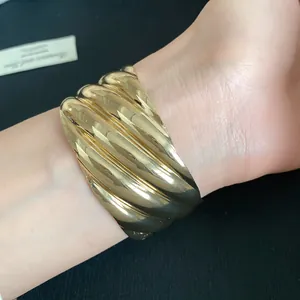 Detailed view of a bold gold-tone wavy-textured metal cuff bracelet worn on the wrist