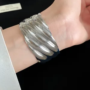Detailed view of chunky silver wave textured metal cuff bracelet worn on a model's wrist.