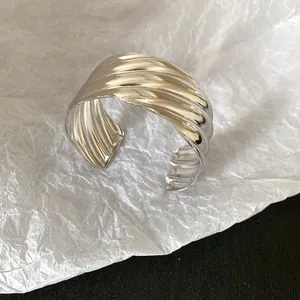 Close-up of a silver-tone metal cuff bracelet featuring bold wave texture details.