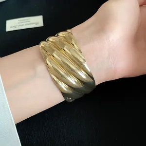 Detailed view of a wide golden metal cuff bracelet featuring bold wavy texture on wrist