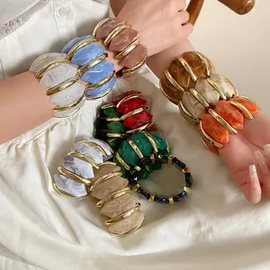 Detailansicht von bunten unregelmäßigen Acryl-Diamant-Armbändern an den Handgelenken.