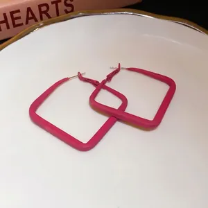 Vibrant hot pink square hoop earrings with silver needle on white plate