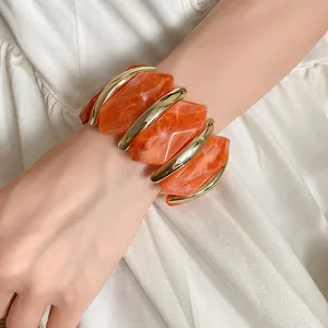 Nahaufnahme eines orangefarbenen Acryl-Armbands mit eleganten goldfarbenen Metallelementen