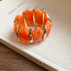 Nahaufnahme des lebhaften orangefarbenen Acryl-Stretch-Armbands mit Goldakzenten