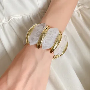 Nahaufnahme eines weißen Marmor-Acryl-Armbands mit unregelmäßigen goldenen Details.