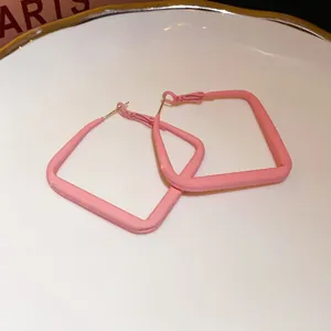 Detailed view of pink square geometric hoop earrings on a white decorative plate.