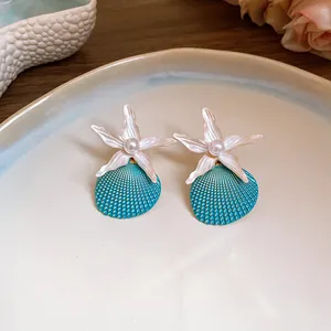 Detailed view of turquoise shell and white starfish stud earrings with a central pearl.
