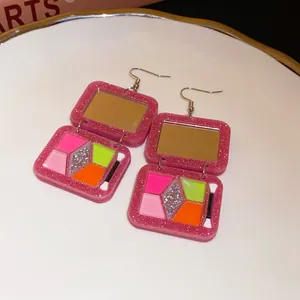Macro view of pink glitter acrylic eyeshadow palette earrings with colorful inserts.