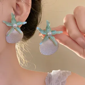 Detailed close-up of light green starfish and textured shell earrings with a center pearl