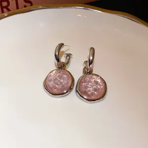 Close-up of elegant pink textured stone drop earrings with silver hoops on white plate