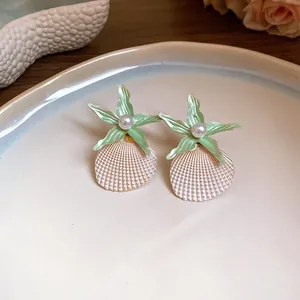 Macro detail of light green starfish and pearl shell earrings on a white ceramic plate.