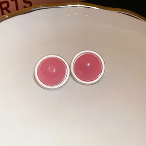 Close-up detail of sweet pink round stud earrings with a white border on a white ceramic dish