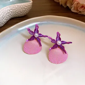 Detailed close-up of purple starfish and pink shell earrings with central pearl accents