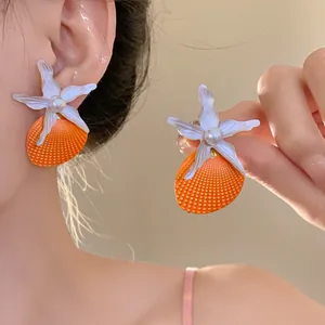 Close-up of orange shell and starfish earrings with pearl center on model's ear