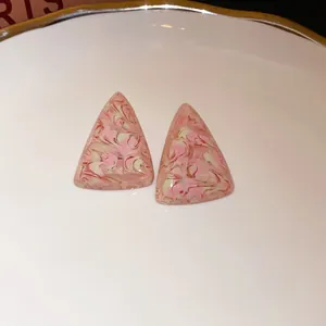 Detail shot of pink and white marbled triangle geometric stud earrings on a gold-rimmed plate