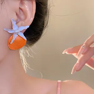 Detail view of starfish and orange shell earring with a pearl on an Asian model's ear.