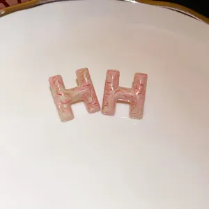 Close-up detail of pink marble textured H-shaped stud earrings on white ceramic dish