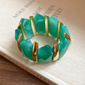 Detailansicht eines grünen elastischen Acryl-Armbands mit goldenen Metallelementen.