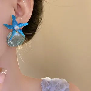 Detailed view of fashionable blue starfish and pearl shell stud earring on model's ear