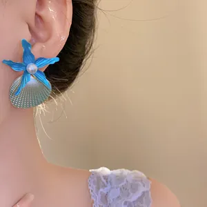Close-up showing a blue starfish and pearl shell earring worn on a model's ear.