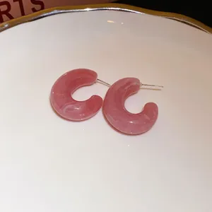 Elegant pink marble resin C-shaped stud earrings displayed on white ceramic dish