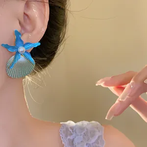 Detailed close-up showing blue starfish and shell earrings with pearls on a female model.