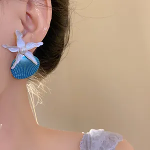 Close-up detail of stylish starfish and blue shell earrings with pearl on model's ear