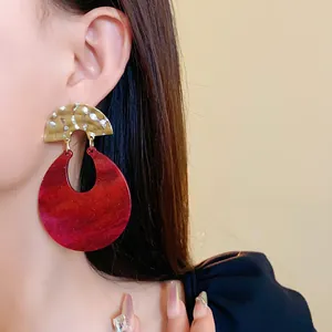 Detailed close-up of vintage red marbled resin U-shaped earrings with gold hammered finish