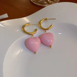 Macro view of elegant pink heart dangle earrings with golden hoops on a white dish